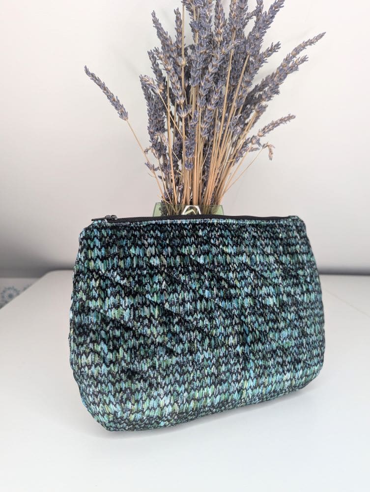 a green and black woven fabric zipper pouch in front of dried lavender