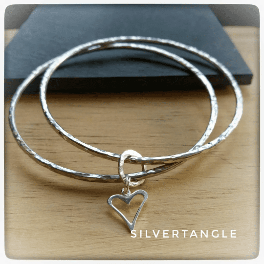 Two Silver bangles joined together with an open heart charm, the bangles are a hammered texture