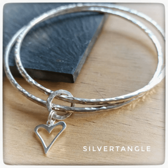 Two Silver bangles joined together with an open heart charm, the bangles are a hammered texture