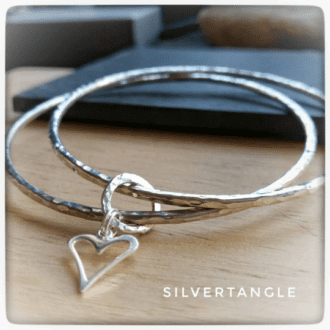 Two Silver bangles joined together with an open heart charm, the bangles are a hammered texture