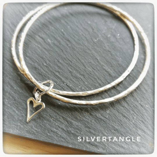 Two Silver bangles joined together with an open heart charm, the bangles are a hammered texture