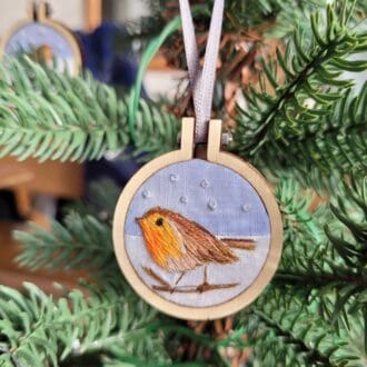 Mini hand embroidered robin sat on a twig in the snow amoungst snowflakes set in a 2.5 cm mini embroidery hoop for Christmas tree decoration.