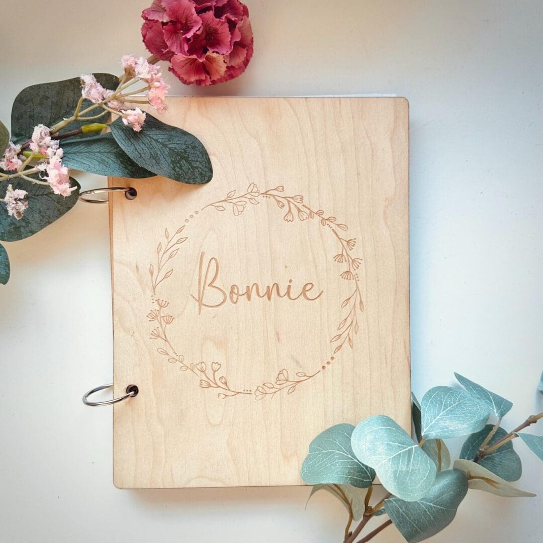 Personalised wooden keepsake notebook with laser-engraved floral wreath design and customisable wording on the cover, featuring an eco-friendly FSC-certified wood finish, plain A5 sheets, and a matching personalised wooden ruler