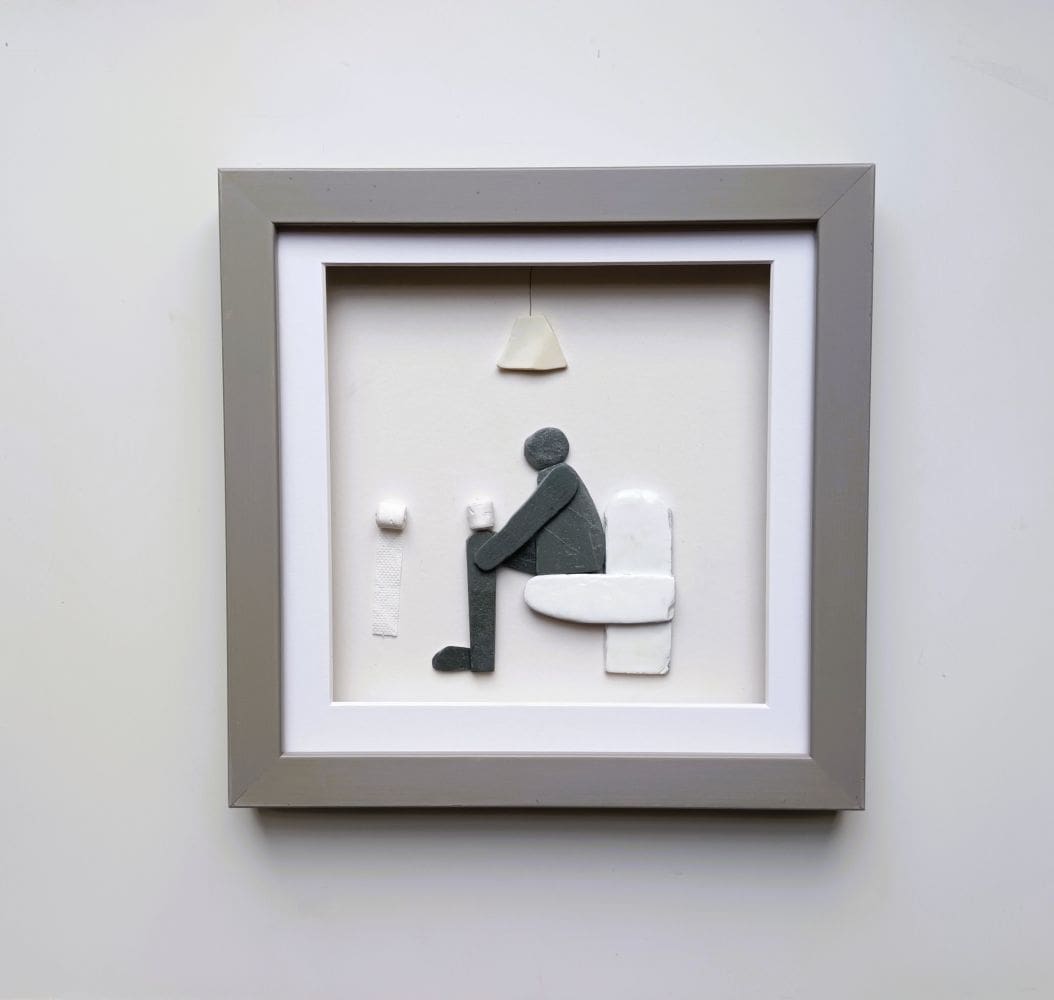 framed picture of man sitting on toilet made from pebbles