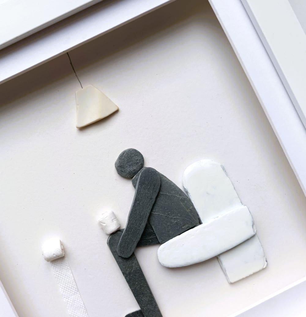 framed picture of a man sitting on the toilet made from pebbles