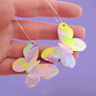 A pair of delicately patterned pastel butterflies hand from 2 fine silver hoops being gently held in a hand