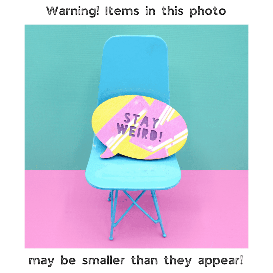 "A vibrant faux leather brooch with 'Stay Weird!' text sits on a miniature turquoise chair against a pink and mint green background, with the text around a white border reading. Warning! Items in this photo may be smaller than they appear.