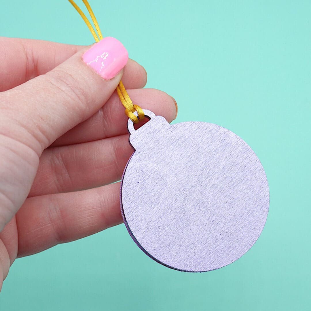 Metallic purple painted rear of a small flat Christmas decoration, held in hand by the gold cord