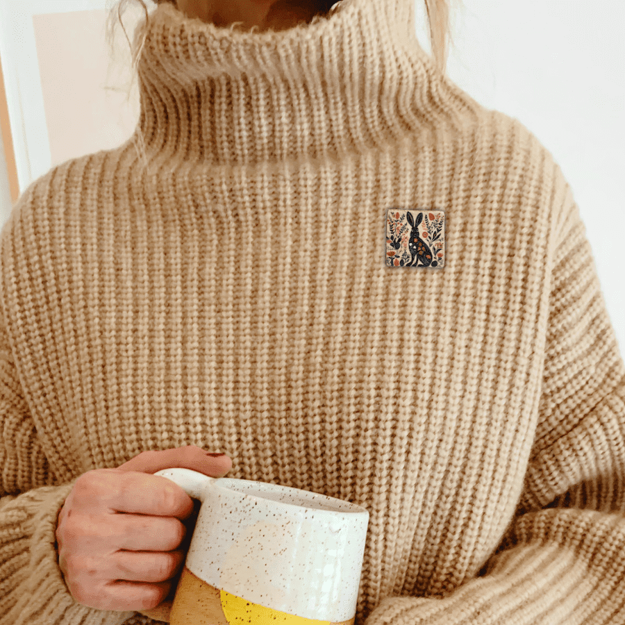 A handmade clay hare brooch being worn on a cosy sweater.