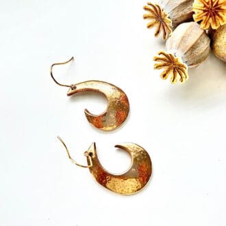 Bronze earrings in a half moon shape with stainless steel gold plated ear wires. Lay on a white surface.