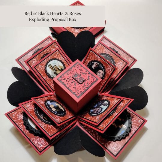 The image shows a red and black themed 'Exploding Proposal Box' with hearts and roses. The box is designed to open up and reveal multiple compartments and decorations, typically used for a marriage proposal or a romantic gesture. The intricate design and the use of hearts and roses make it visually appealing and relevant for special occasions like proposals