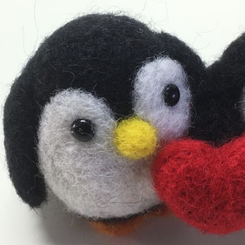 Close-up of one penguin from the needle-felted couple holding a red heart, showcasing detailed features.