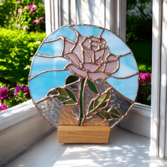 Handmade stained glass candle holder featuring a pink rose with a blue sky background, displayed on a wooden stand. Perfect romantic gift idea for Valentine's Day, engagement present, or rustic home decor.